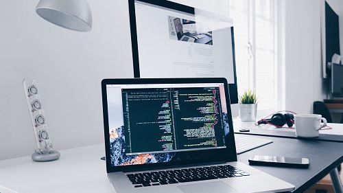a macbook with lines of code on its screen on a busy desk laptop computer e1772099051145